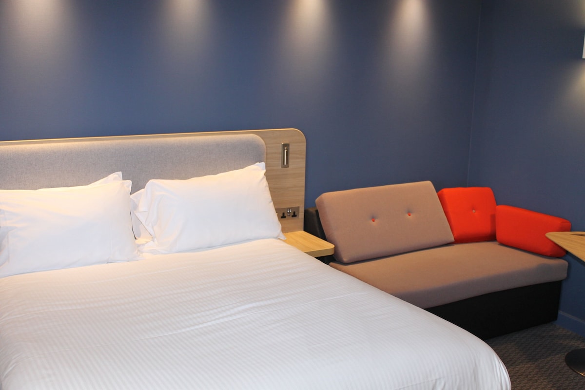 Een hotelkamer met een groot bed, een kleine zithoek en een nachtkastje.
