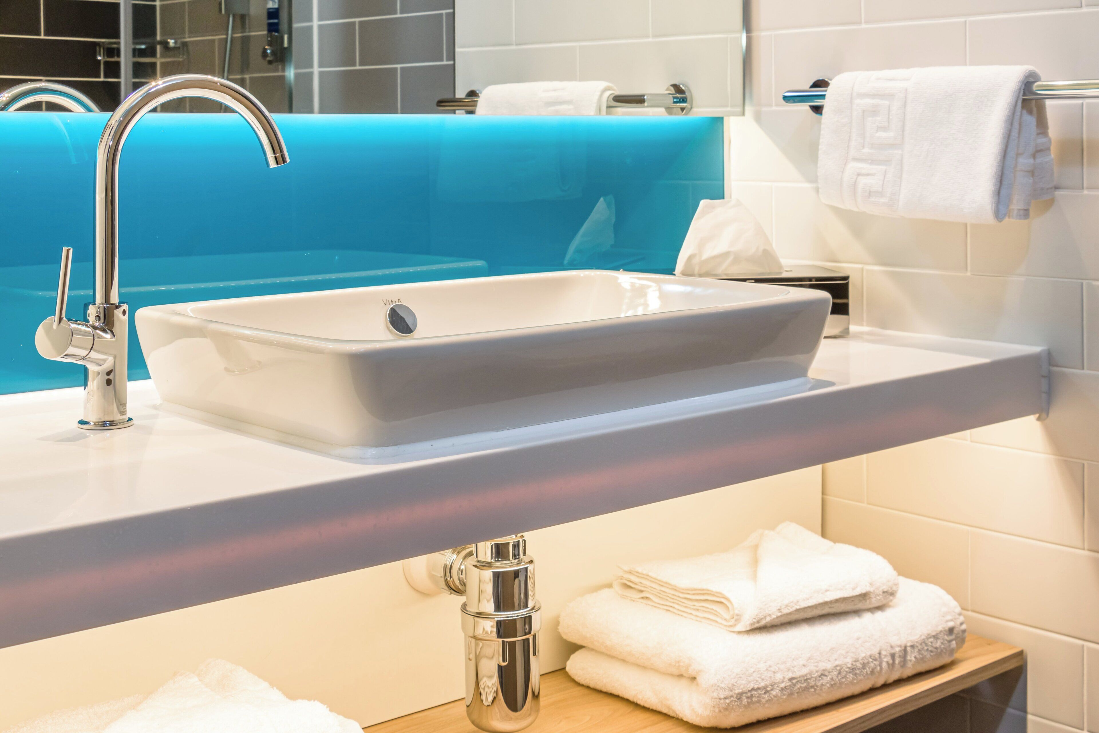 A modern bathroom with a white sink, chrome faucet, and a blue bathtub.
