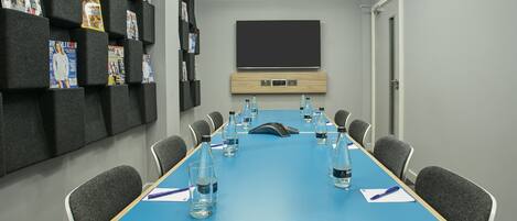 A conference room with a blue table, grey chairs, water bottles, and magazines on shelves.