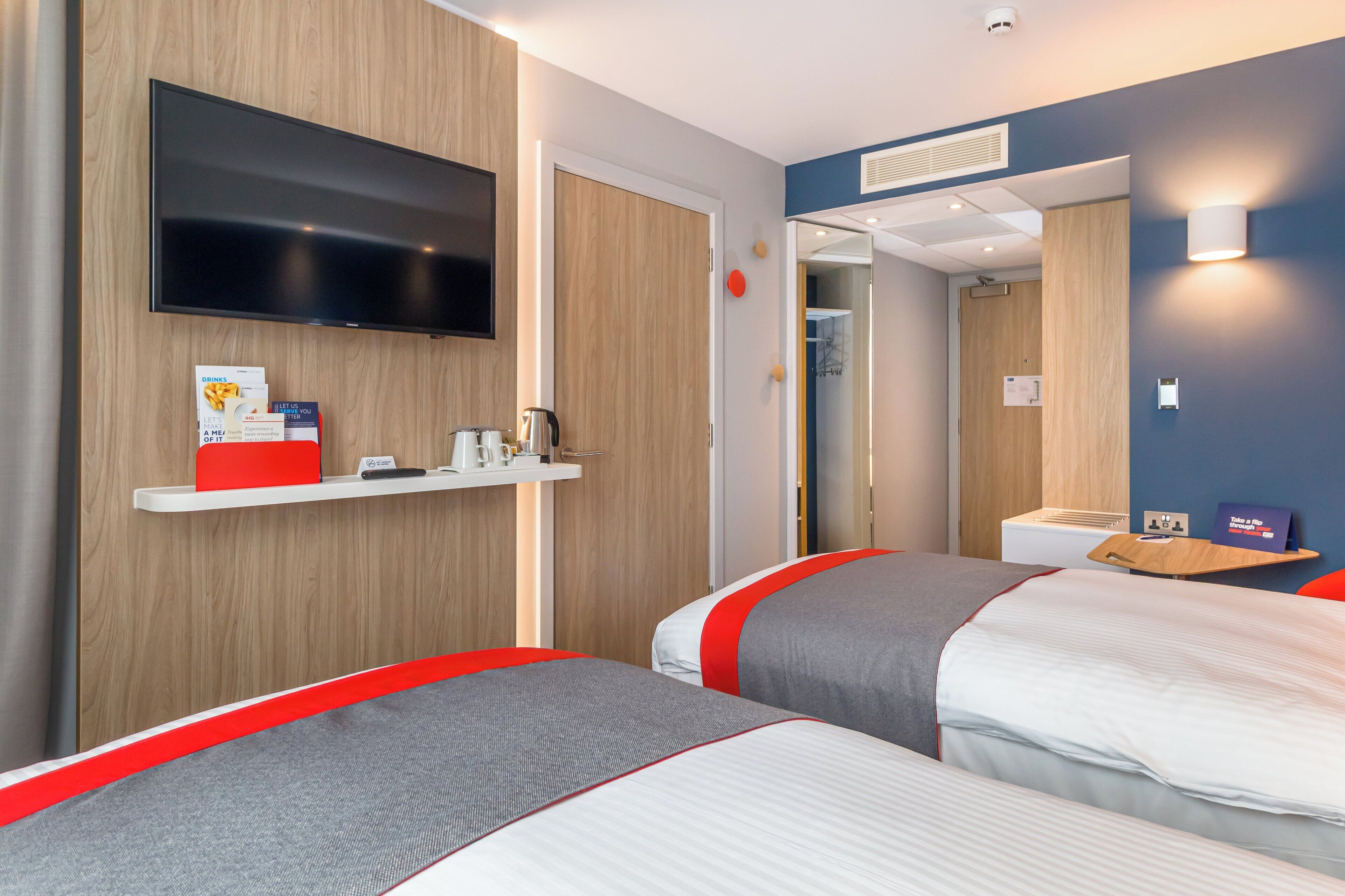 Habitación de hotel con dos camas, un televisor, un estante con artículos de cortesía y un espejo.