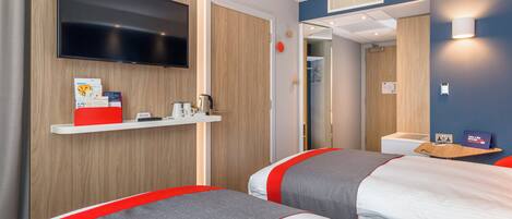 Habitación de hotel con dos camas, un televisor, un estante con artículos de cortesía y un espejo.