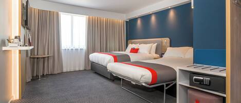 A hotel room with two beds, a TV, a small table, and a storage bin.