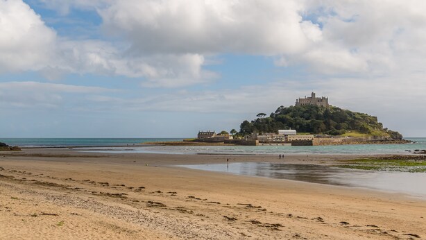 A beach with a castle on a hill, clear sky, and calm sea. - Holiday Inn Express Bodmin - Victoria Junction by IHG (St Austell)