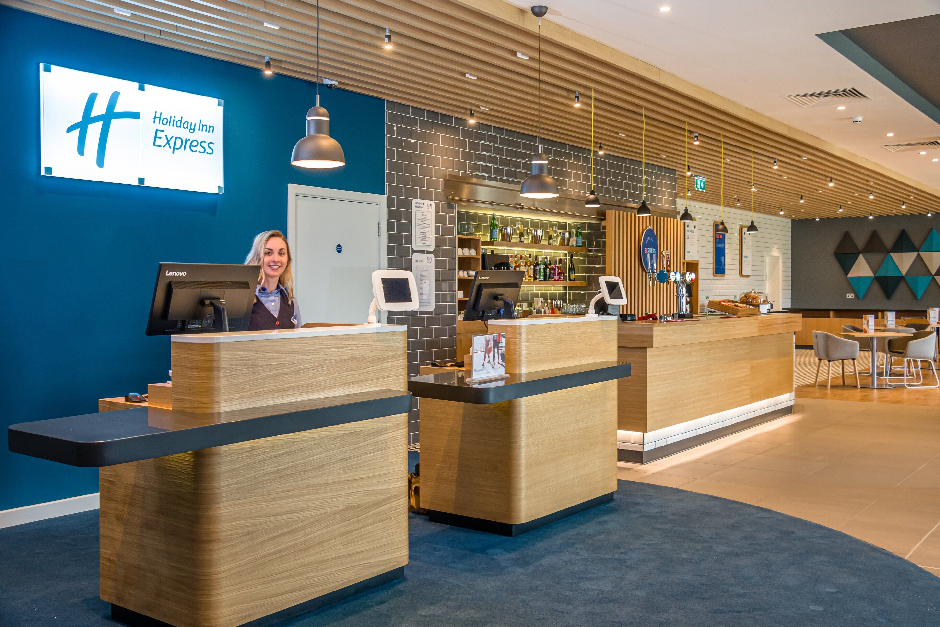 A Holiday Inn Express reception area with a modern design, featuring a reception desk, a bar area, and a seating space.