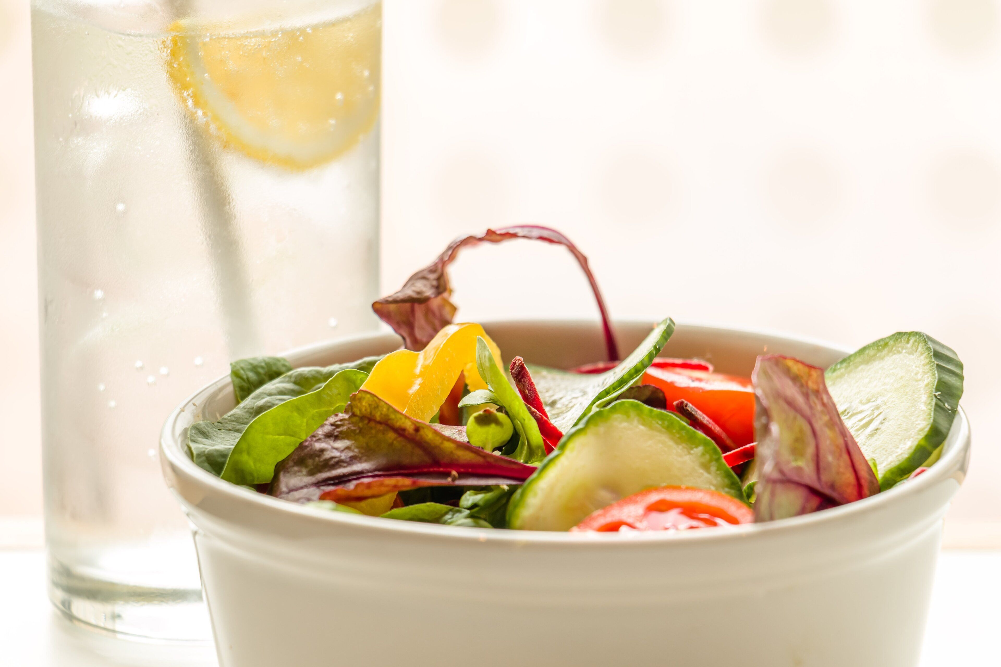 A bowl of salad with various vegetables and a glass of water with a lemon slice.