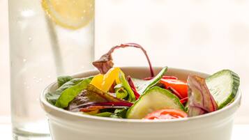 A bowl of salad with various vegetables and a glass of water with a lemon slice.