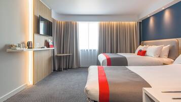 A hotel room with two beds, a TV, a desk with a lamp, and a window with curtains.