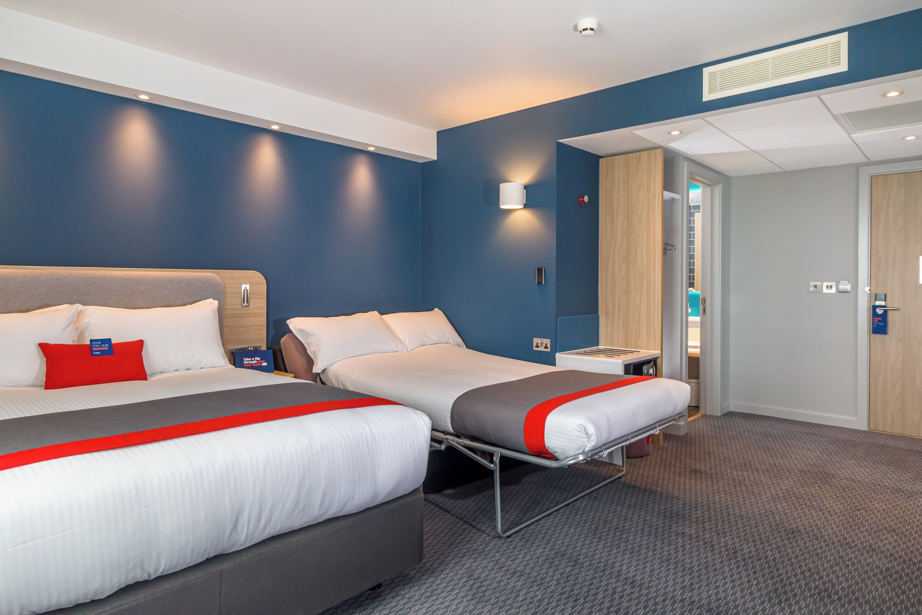 A hotel room with two beds, a desk, a chair, and a wardrobe.