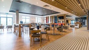 A spacious indoor area with wooden flooring, multiple tables and chairs, and a patterned rug. - Holiday Inn Express Bodmin - Victoria Junction by IHG (St Austell)
