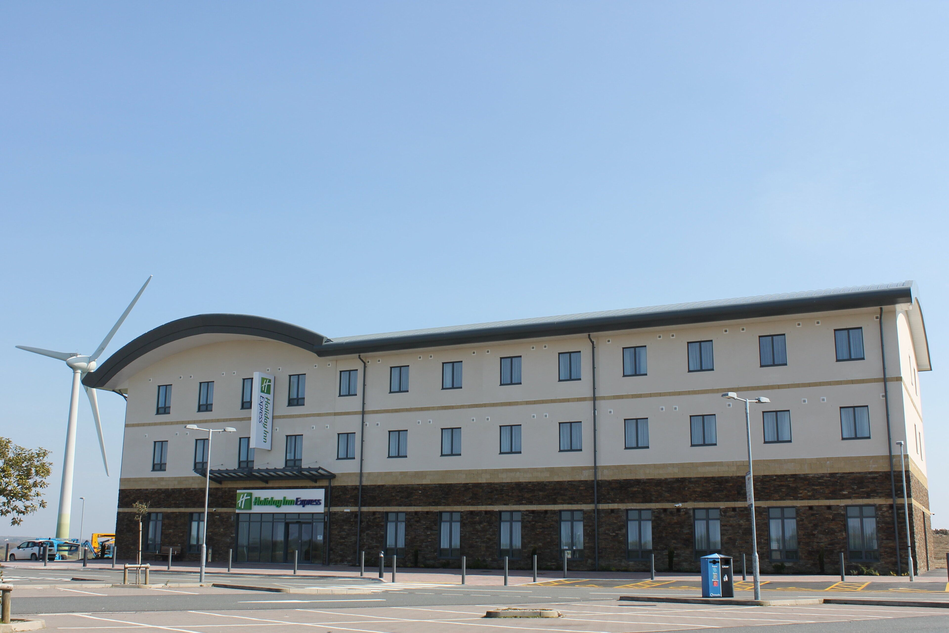 A modern hotel with a curved facade, multiple windows, and a wind turbine in the background.