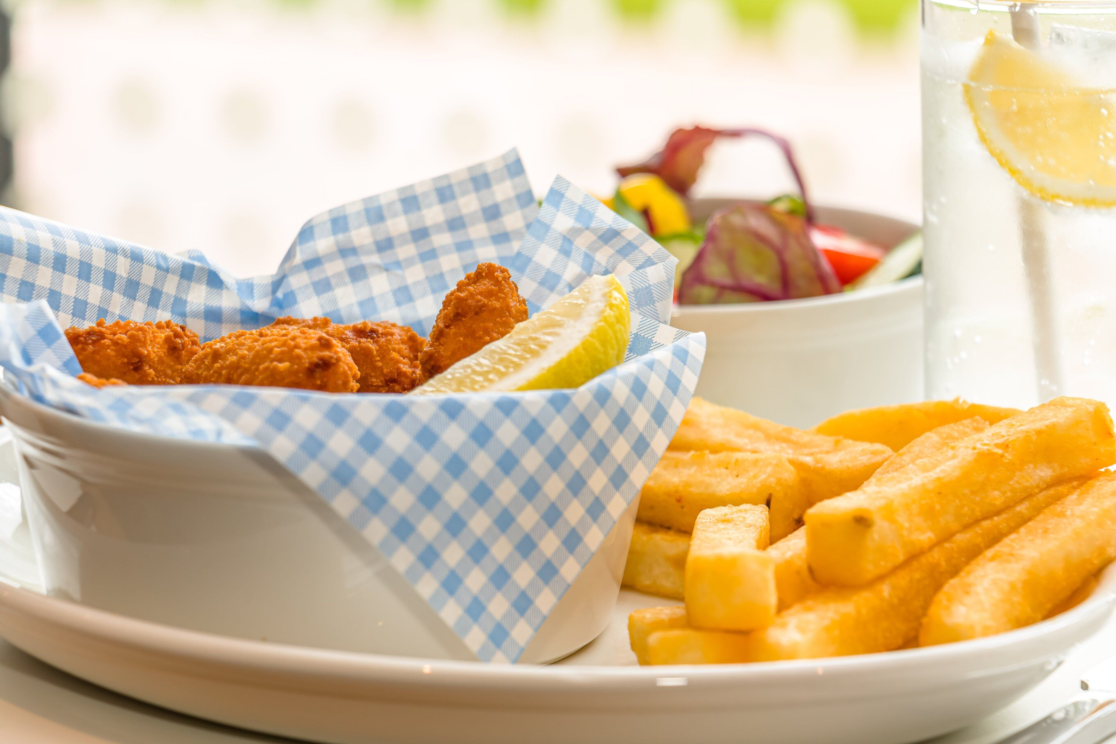 A plate with fried fish and French fries, a glass of lemonade, and a bowl of salad.