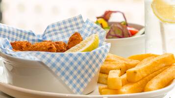 A plate with fried fish and French fries, a glass of lemonade, and a bowl of salad.