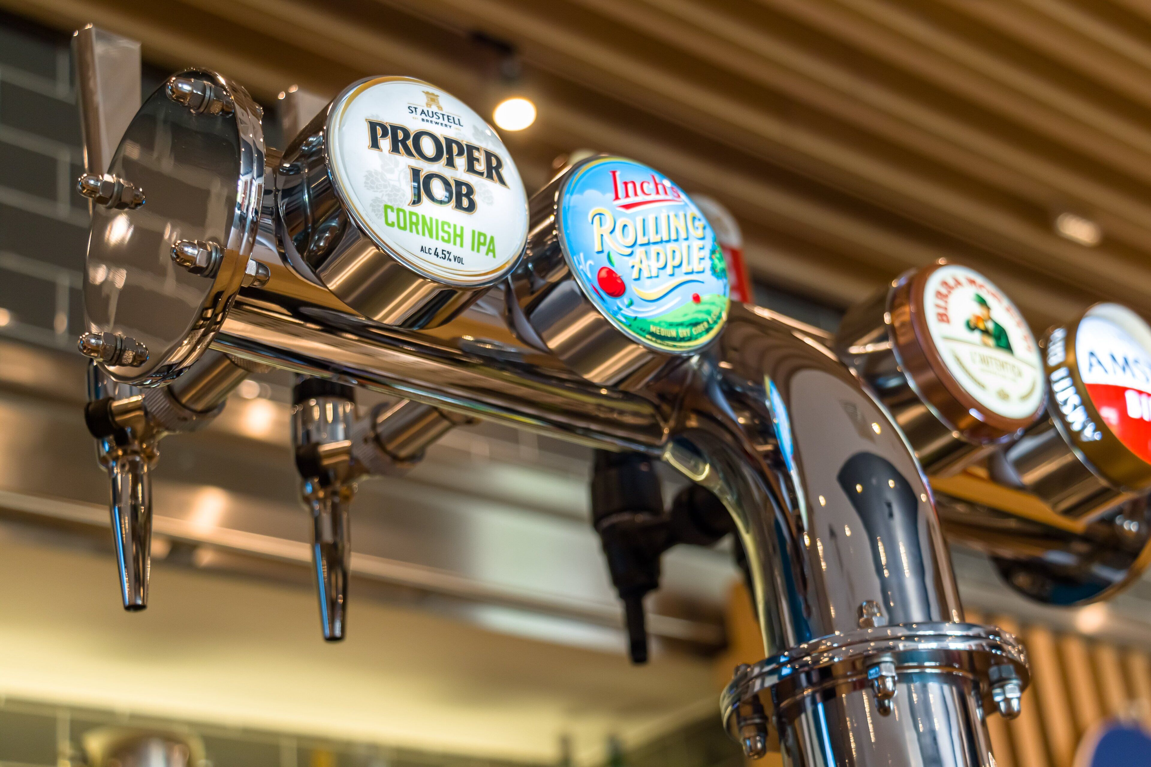 Primer plano de un grifo con etiquetas que dicen 'Proper Job Cornish IPA' e 'Inch's Rolling Apple'.