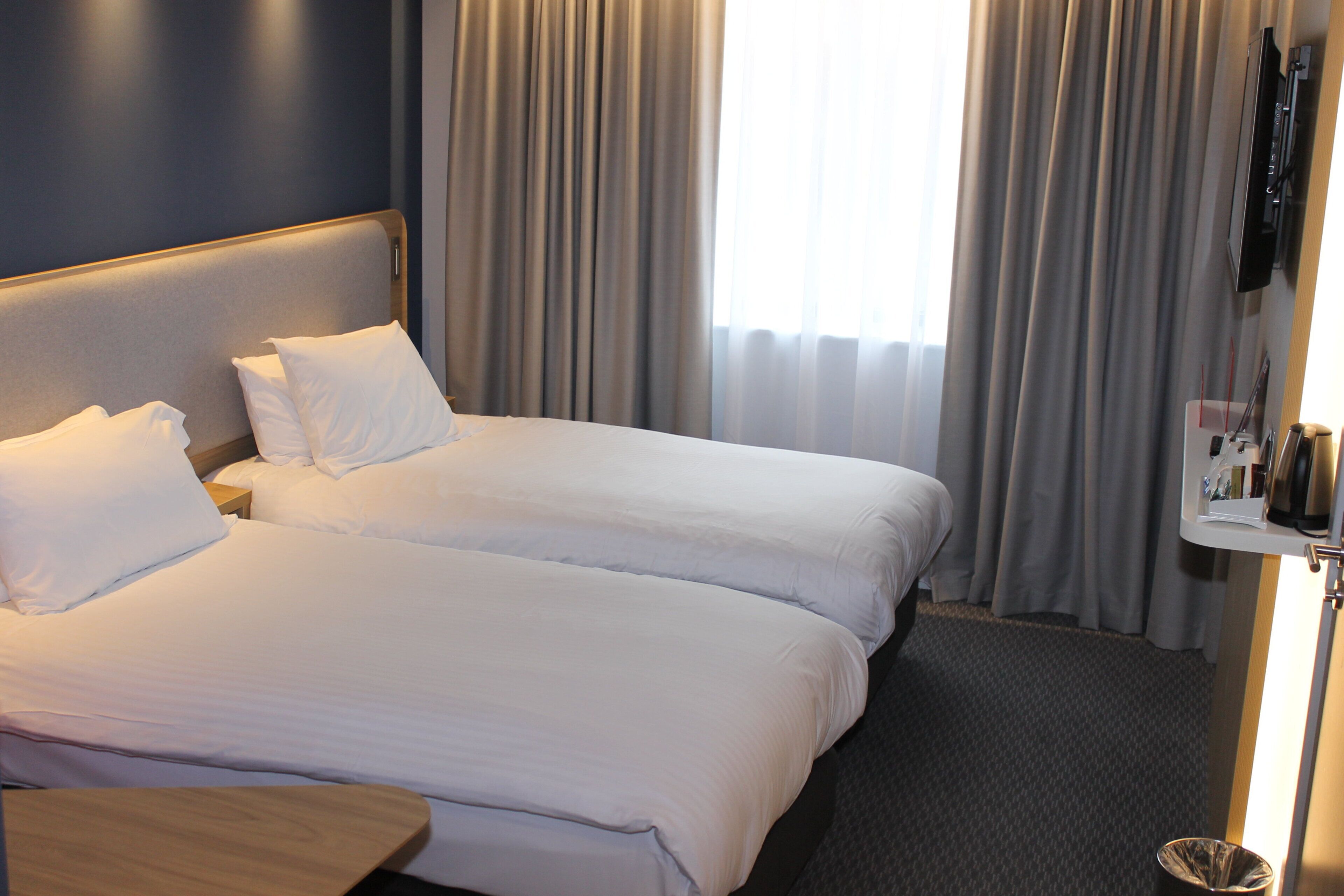 Habitación de hotel con dos camas, una mesita de noche, televisión y ventana con cortinas.