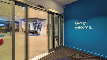 A modern interior with a glass door entrance, a blue accent wall, and a welcoming message.