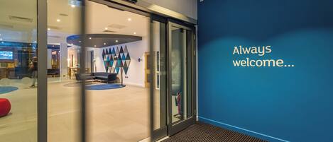 A modern interior with a glass door entrance, a blue accent wall, and a welcoming message.