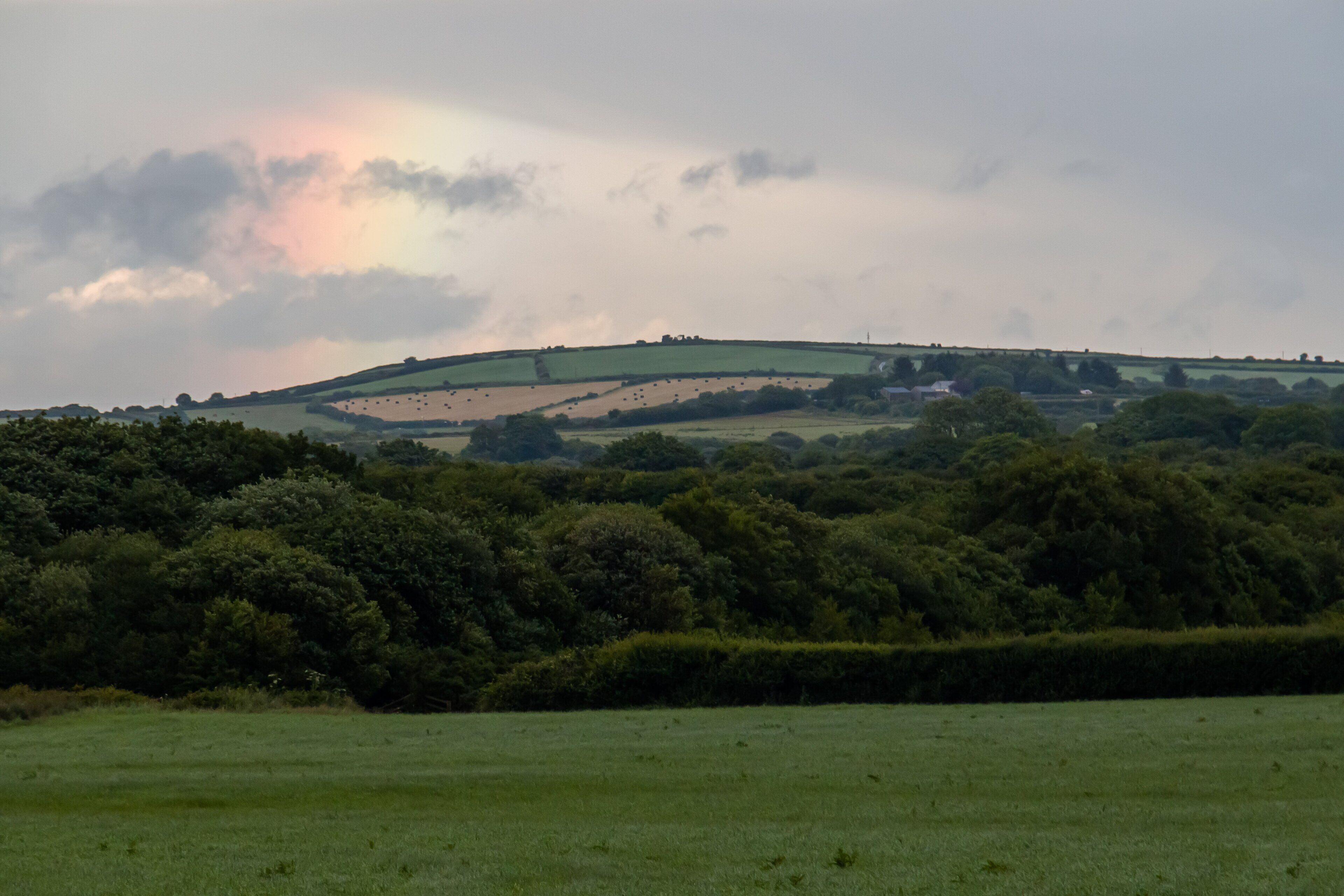 A rural landscape with rolling hills, dense greenery, and a cloudy sky.