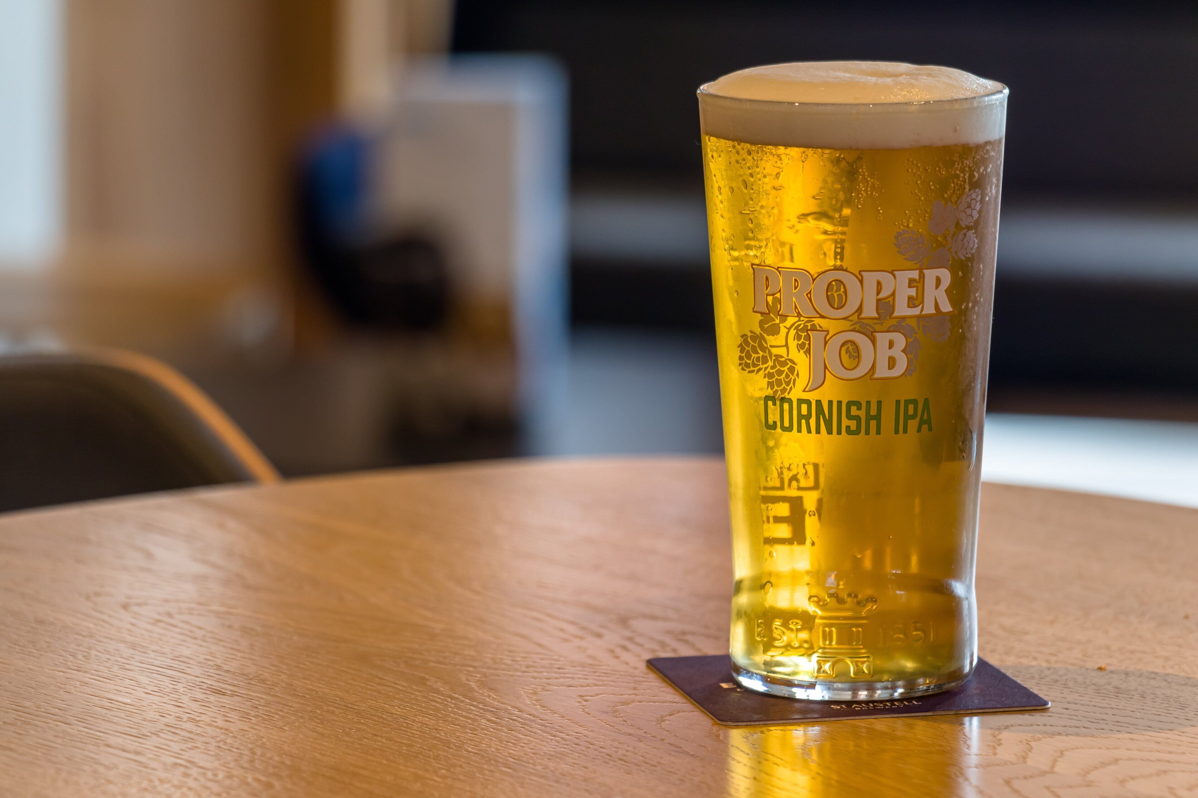 A tall glass of beer on a wooden coaster.