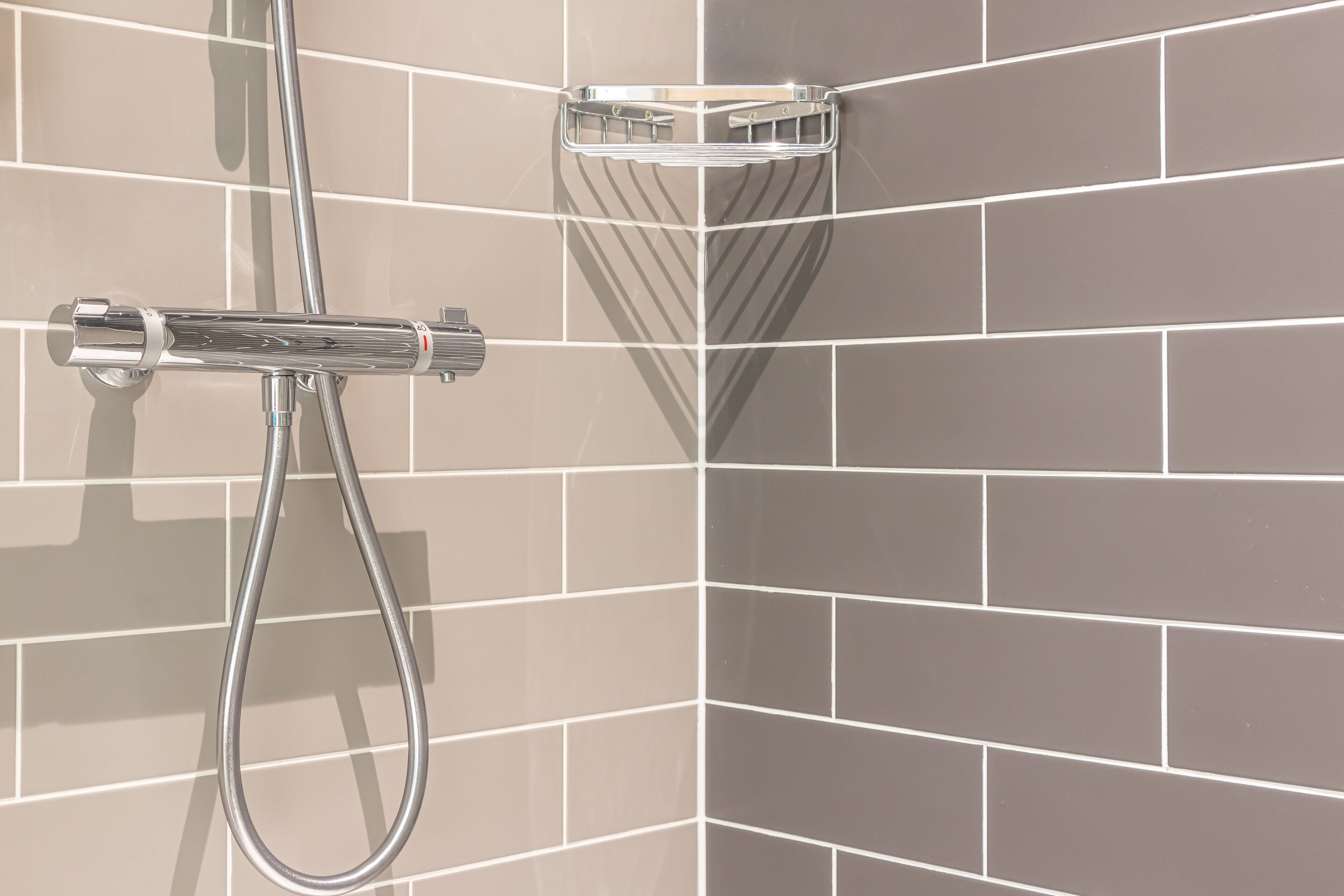 A corner shower with a chrome faucet and a chrome showerhead, set against a tiled wall.