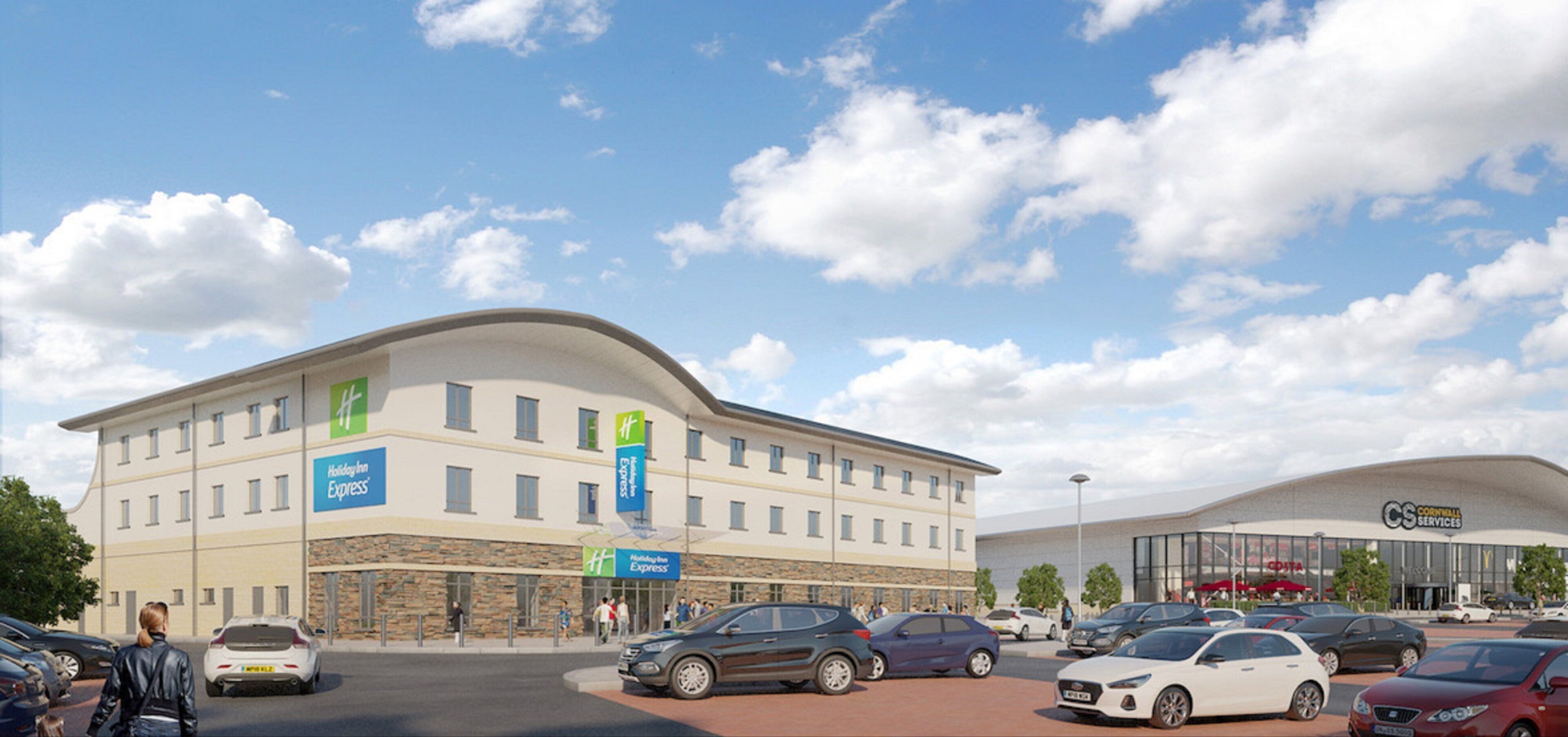 Un hôtel Holiday Inn Express avec un parking rempli de voitures, une façade en pierre et un ciel d’un bleu éclatant.