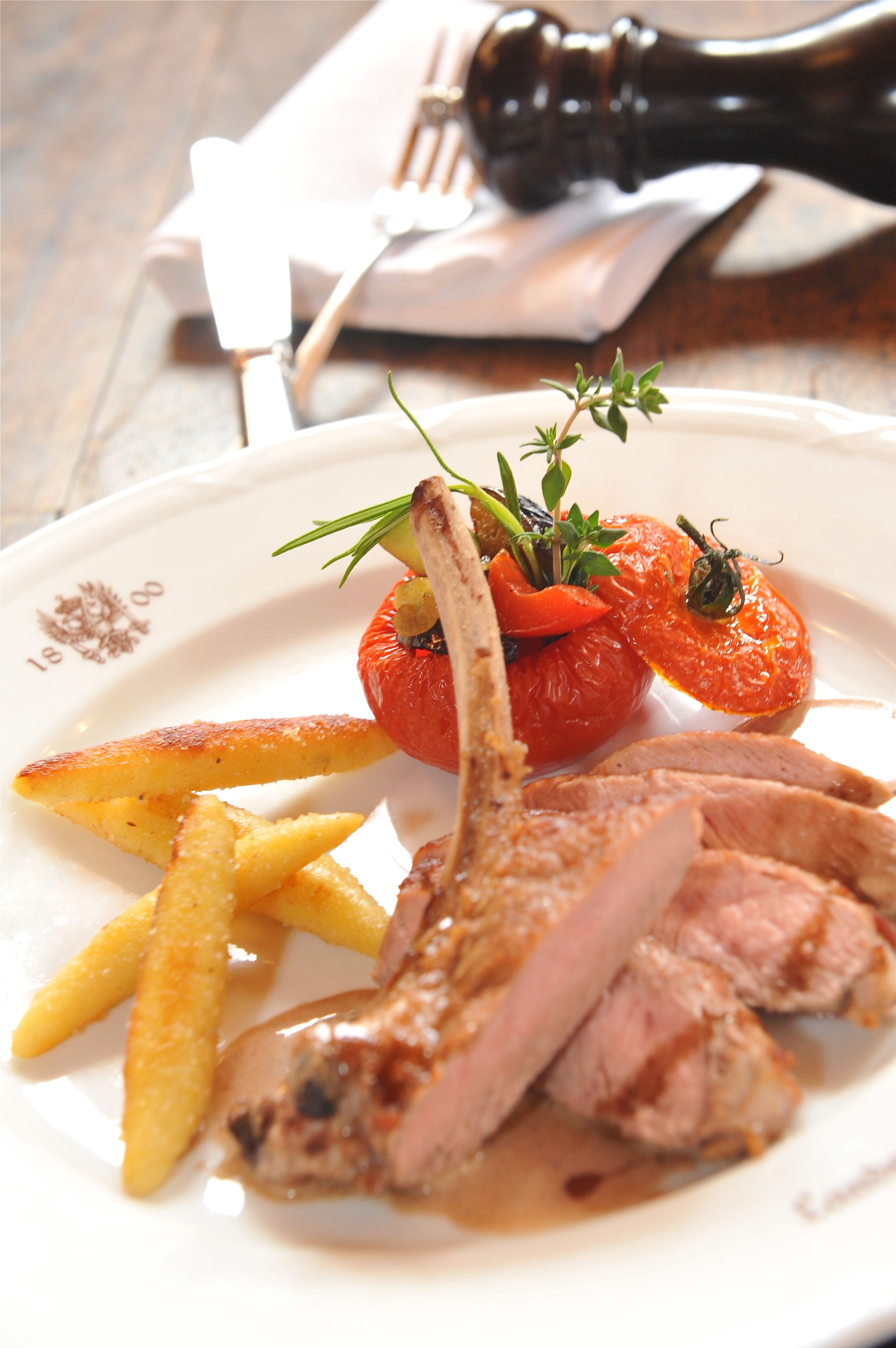 A plate with a lamb chop, roasted tomatoes, and fries.