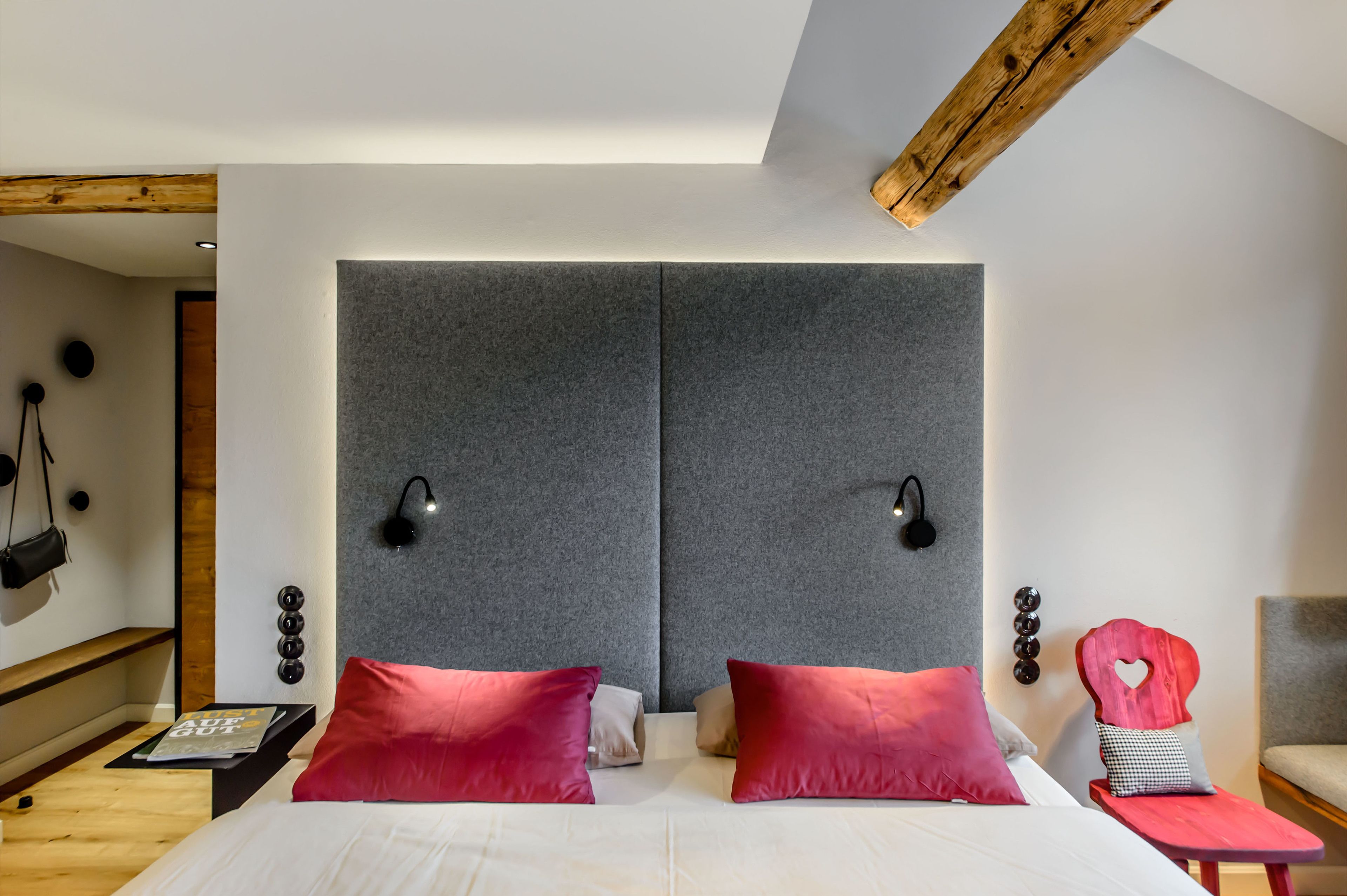 Ein modernes Schlafzimmer mit einem großen Bett, zwei Nachttischen, einem roten Sessel und einem Holzbalken an der Decke.