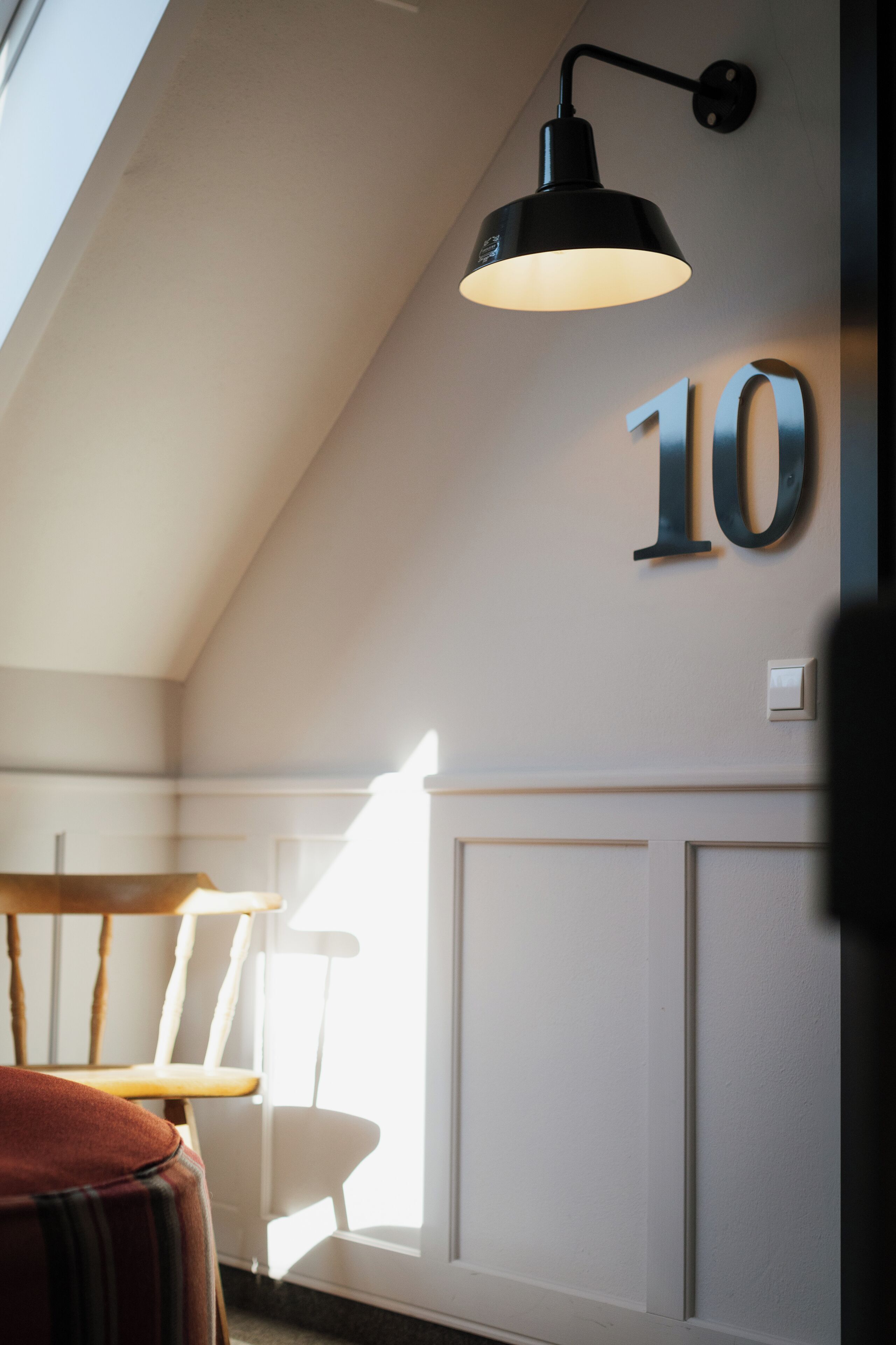 A room with a sloped ceiling, a wall-mounted number '10', a white chair, and a table with a striped cushion.