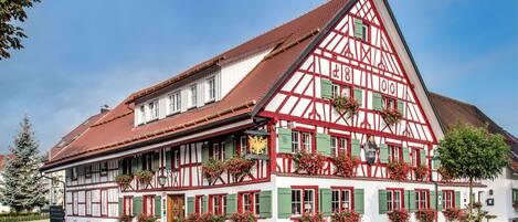 A traditional half-timbered building with multiple windows and green shutters, located at a street corner.