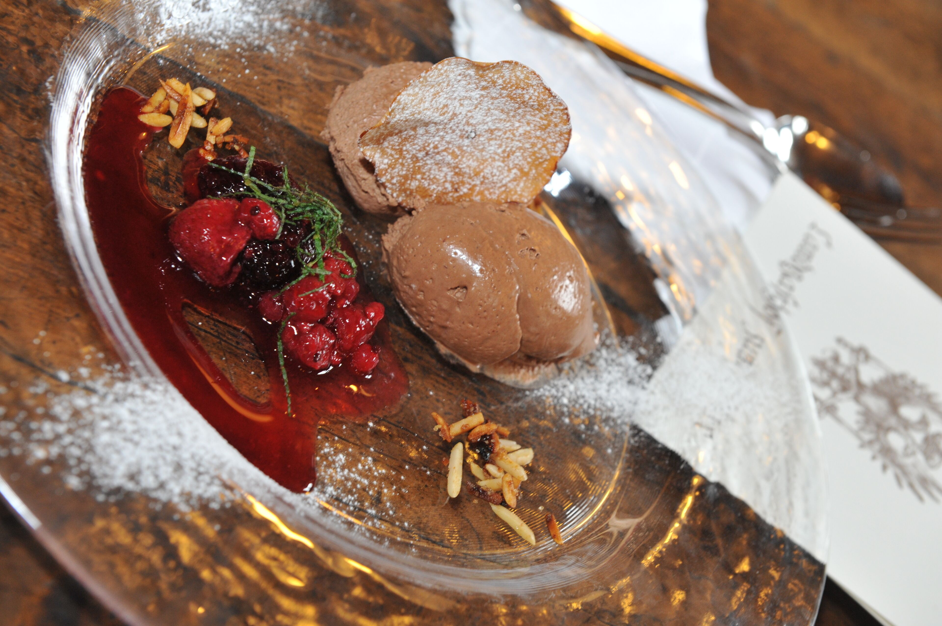 Une assiette à dessert avec un dessert au chocolat, des fruits rouges et du sucre glace.