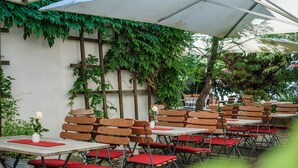 An outdoor seating area with wooden chairs and tables, covered by a white canopy, and surrounded by greenery. - BIO-Hotel Adler (Vogt)