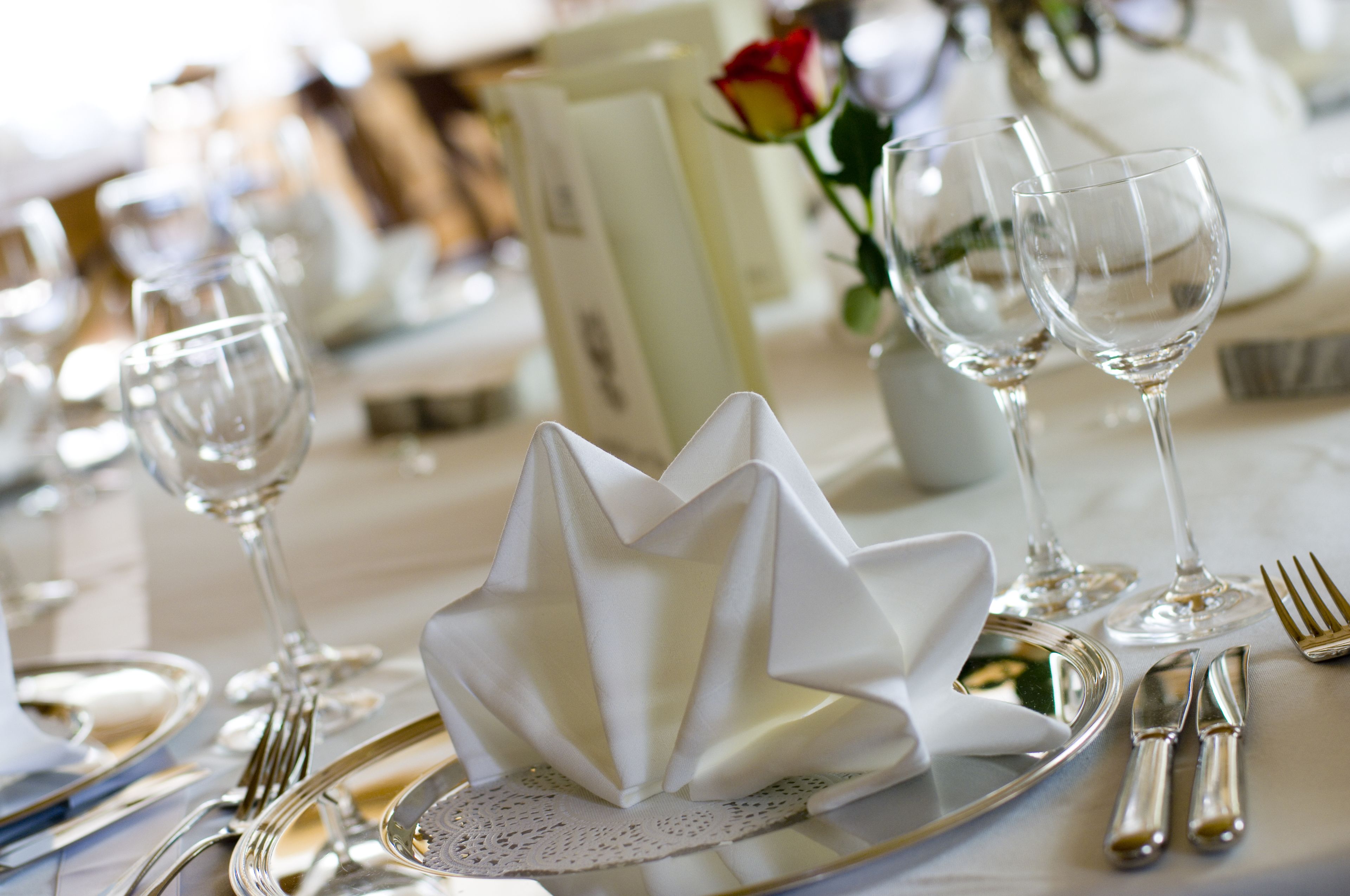 Mesa formal para cenar con mantel blanco, cubiertos y copas de cristal.