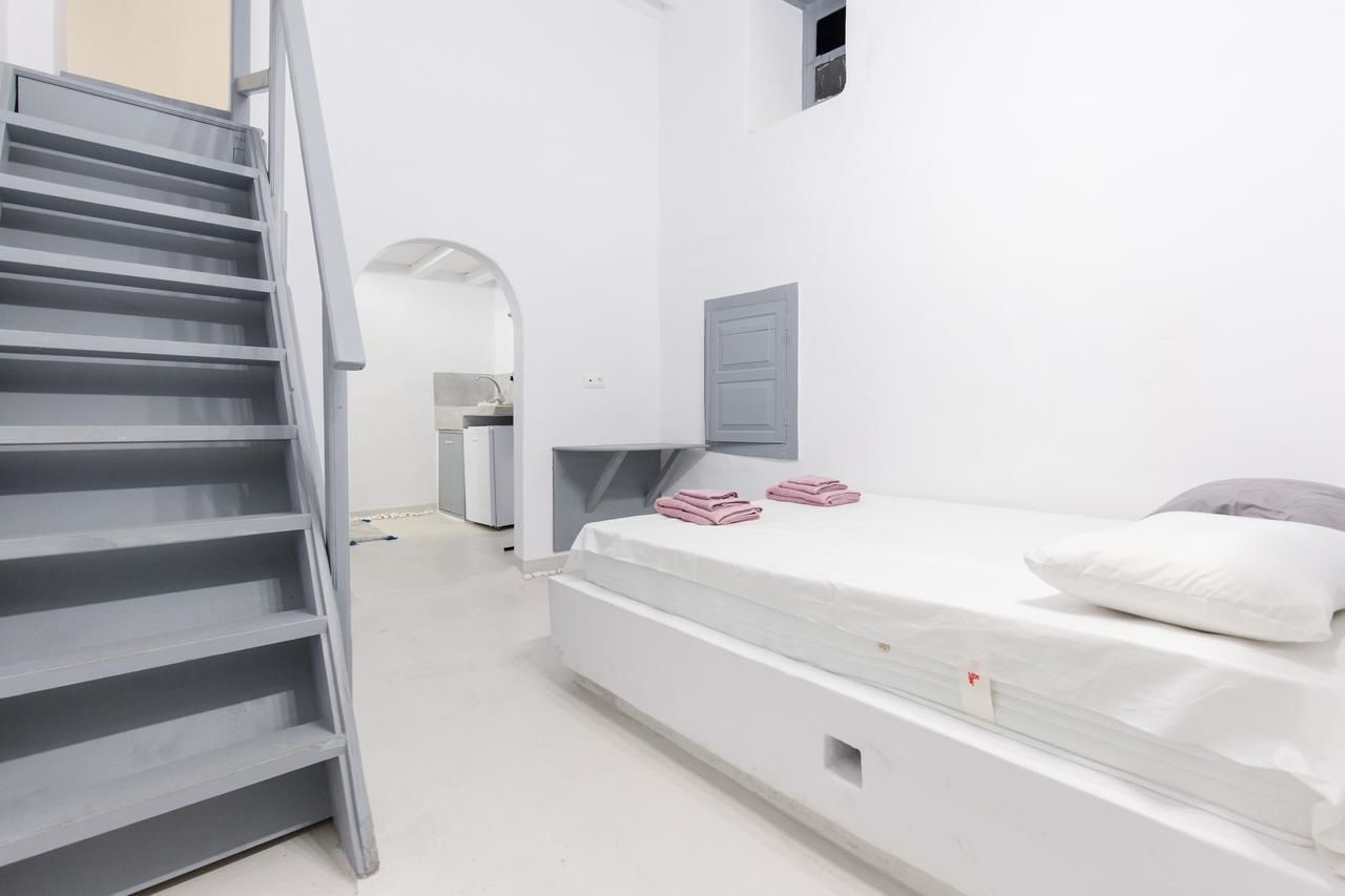 A minimalist bedroom with a bed, a staircase, and a small kitchenette.