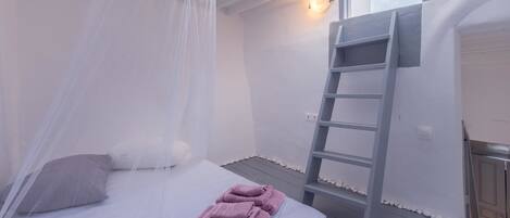 A bedroom with a bed, a ladder, and a window.