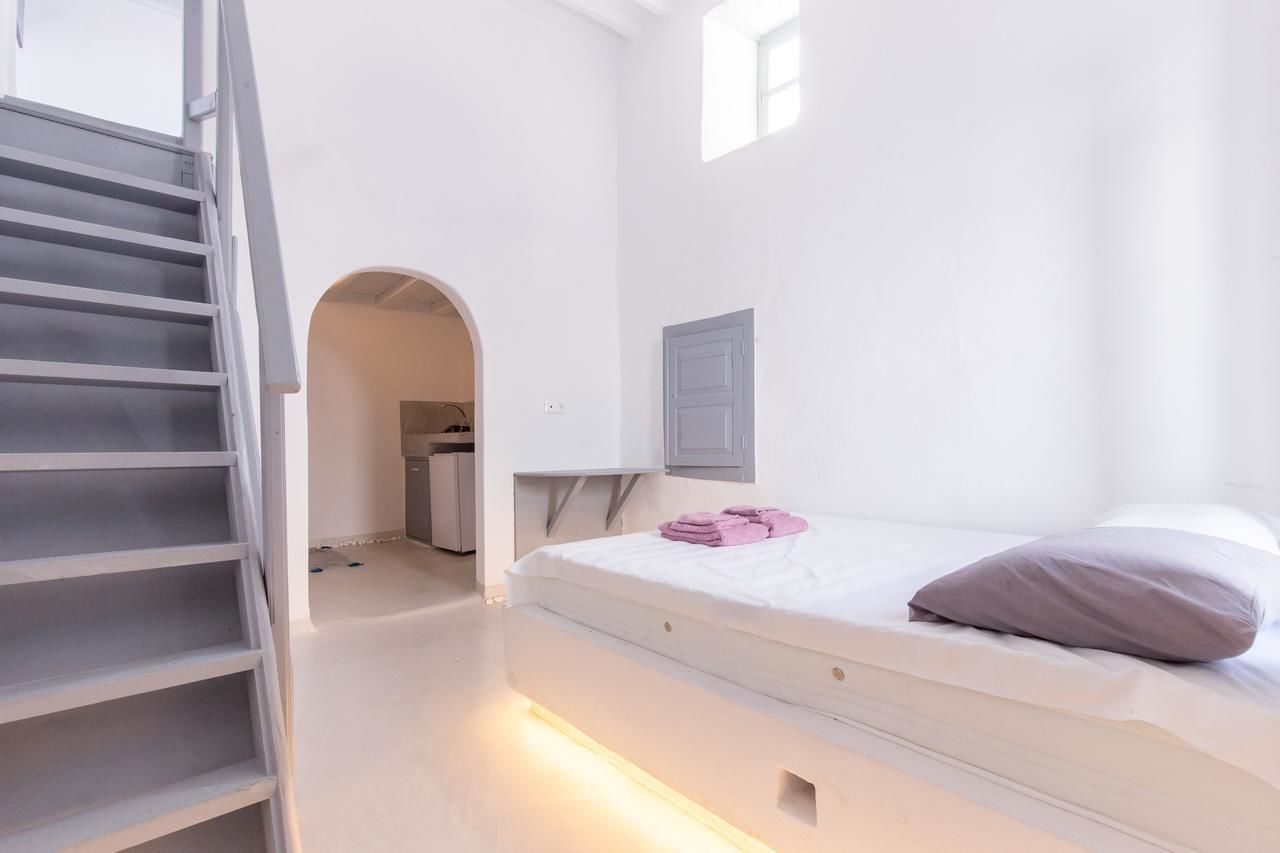 Een minimalistische slaapkamer met een bed, een klein tafeltje, een raam en een trap.