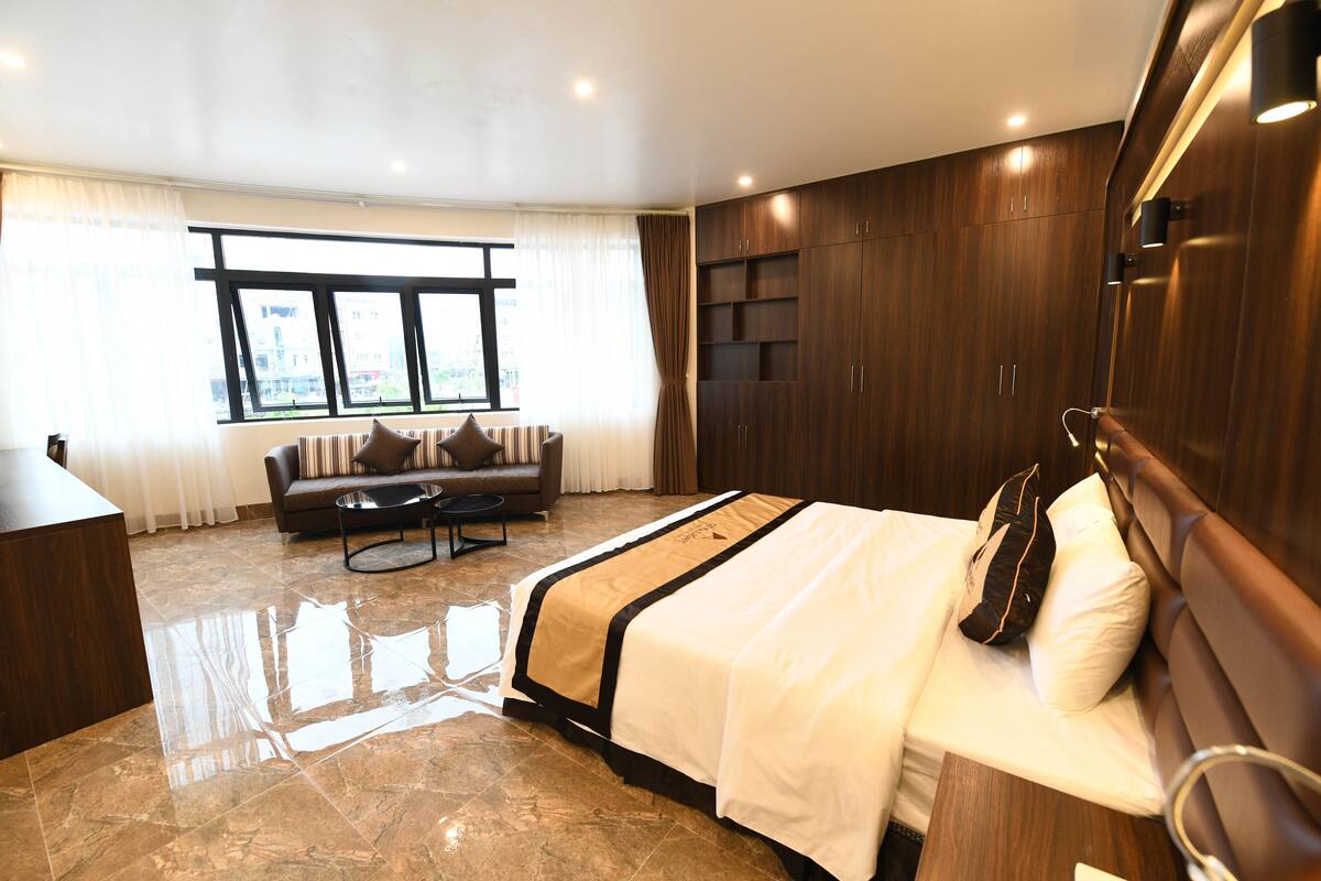 A modern hotel room with a large bed, a sofa, a desk, and a wardrobe.