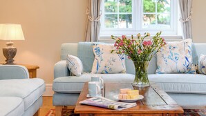 Una sala de estar con un sofá, una mesa de centro con revistas y aperitivos, una lámpara y un jarrón con flores.