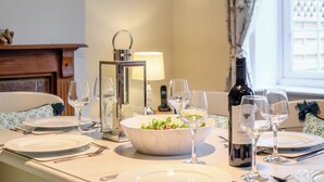 Una mesa lista para comer, con platos, vasos, cubiertos, ensalada en un bol, una botella de vino y una vela.