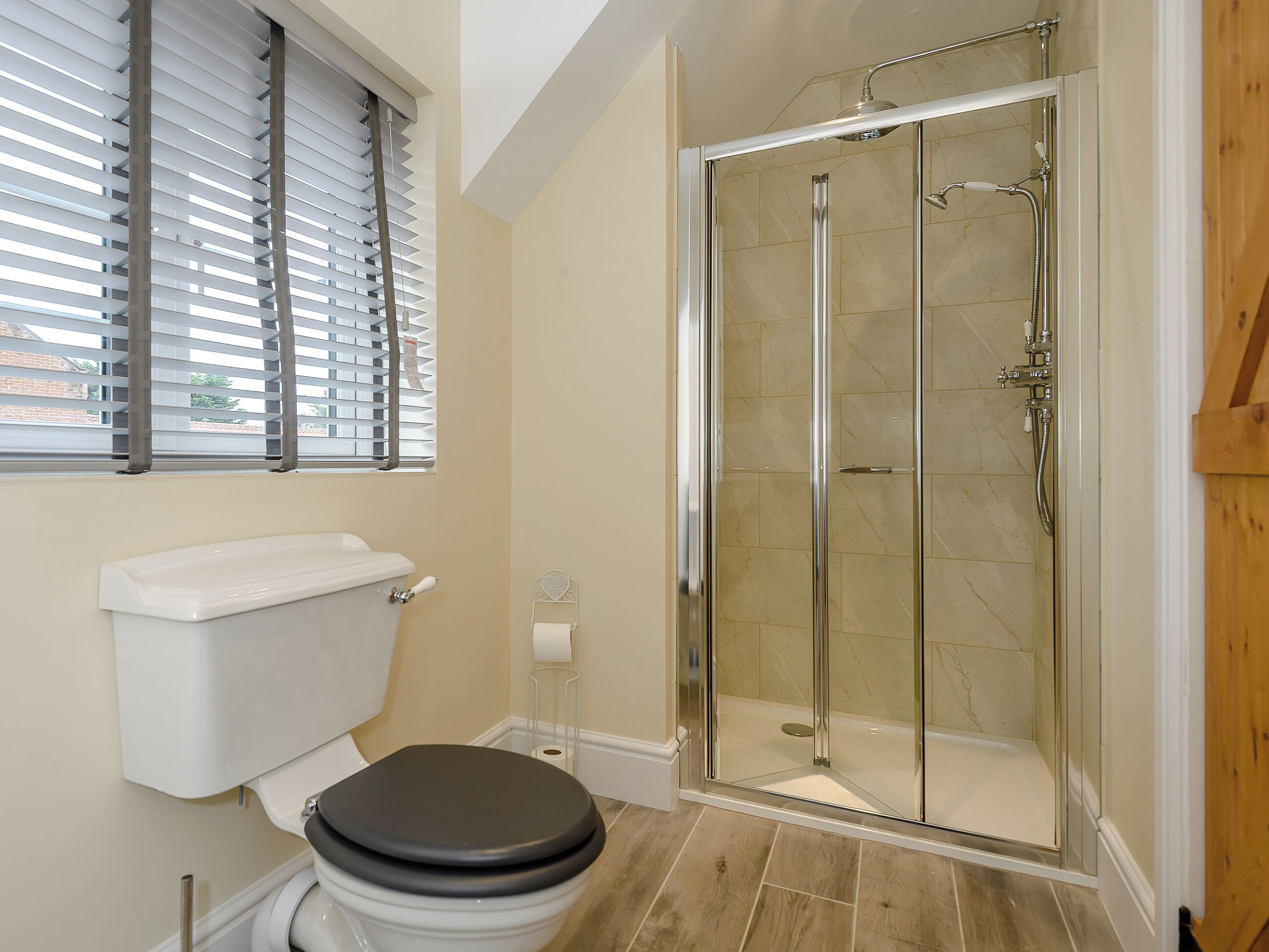 A bathroom with a toilet, a glass shower enclosure, and a window with blinds.