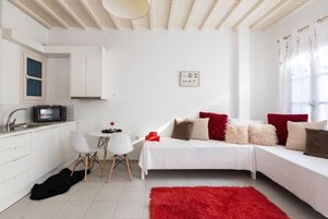 Un espacio habitable moderno, con decoración en blanco, que incluye una kitchenette, un comedor y un sofá con cojines rojo y beige.