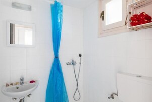 Un baño con lavamanos blanco, ducha con cortina azul y ventana con toallas rojas.