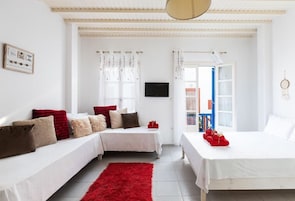 Un dormitorio moderno y bien iluminado, con una decoración en tonos blancos, que incluye dos camas, una alfombra roja y un televisor en la pared.