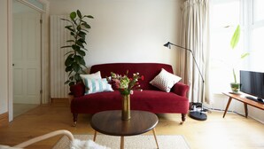 Een woonkamer met een rode bank, een ronde houten salontafel, een potplant en een televisie op een houten dressoir.