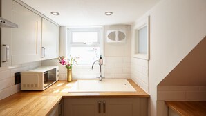 Een kleine keuken met witte kasten, een houten aanrecht, een magnetron, een spoelbak en een raam met uitzicht.