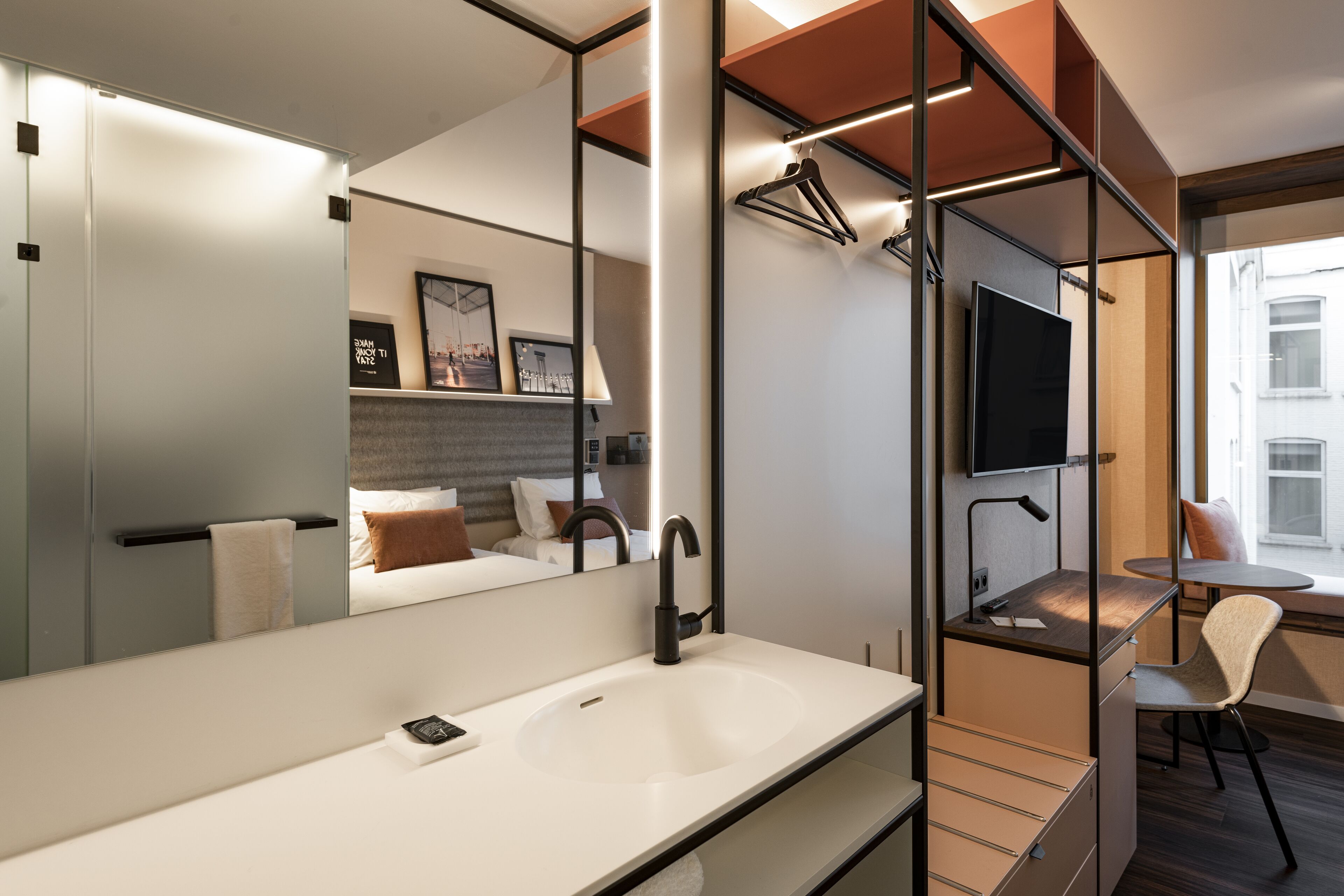 A modern hotel bathroom with a large mirror, a sink, and a television.