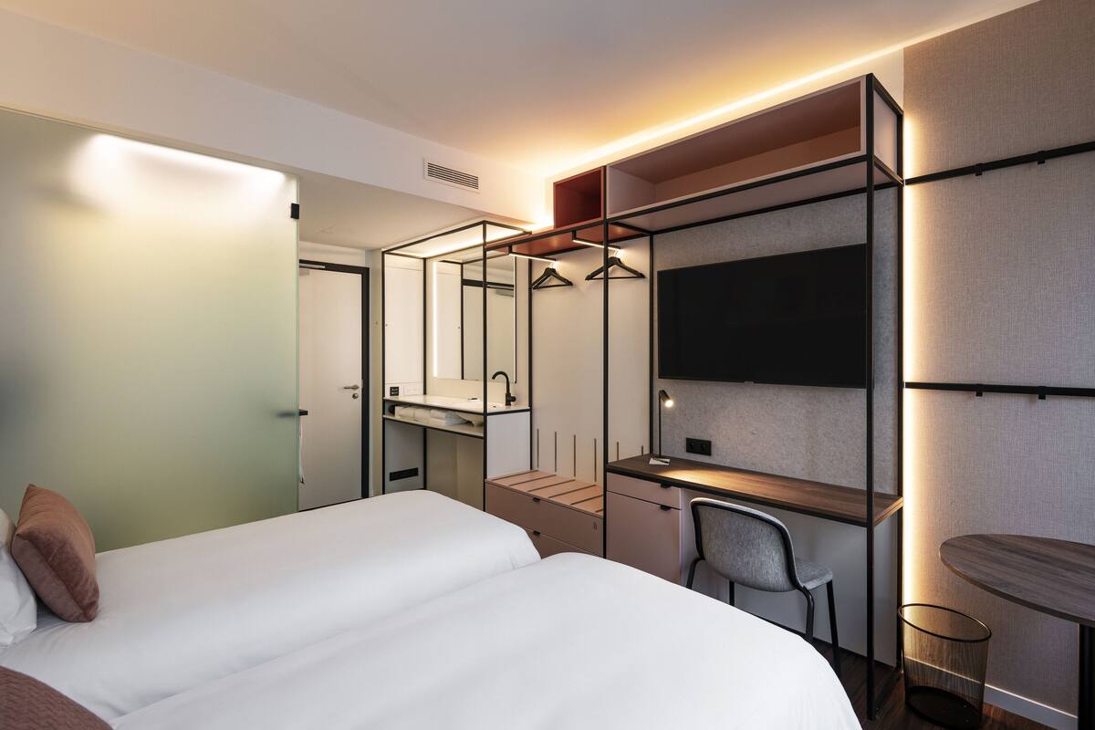 Une chambre d’hôtel moderne équipée d’un lit, d’un bureau, d’une chaise, d’un miroir et d’une télévision.