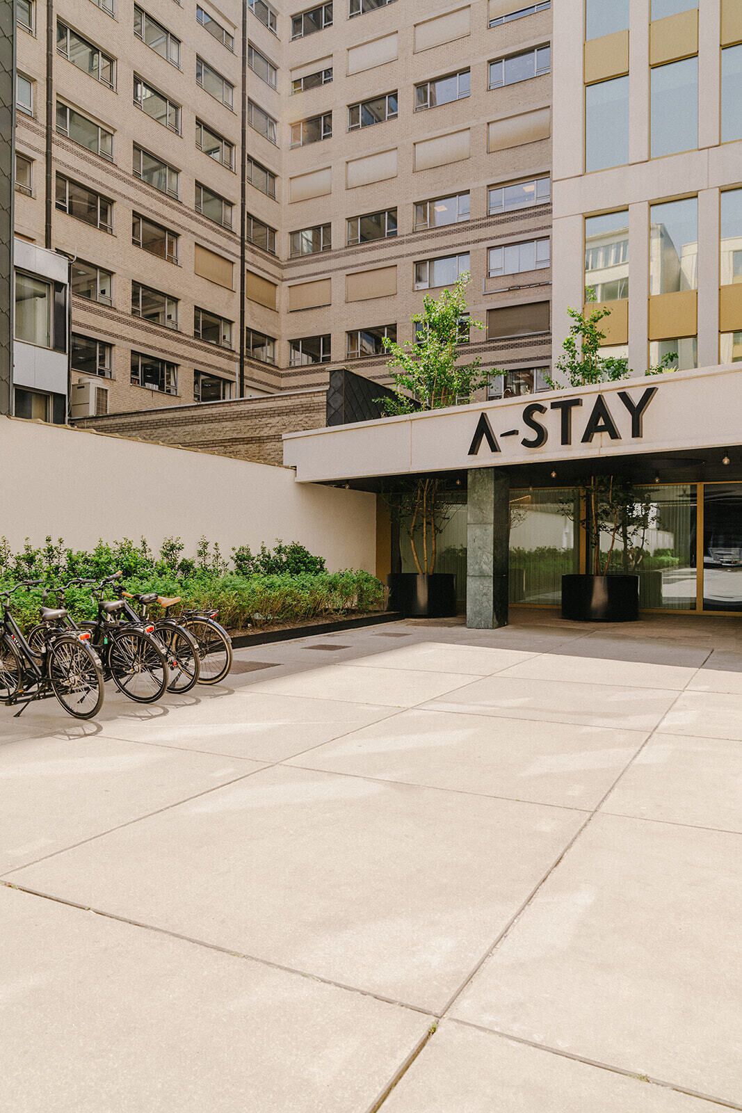 A modern building with a sign reading 'A-STAY' and a bike parking area in front.