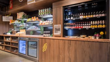 A bar area with a wooden counter, shelves stocked with snacks and condiments, a refrigerated display case, and a selection of bottled beverages.