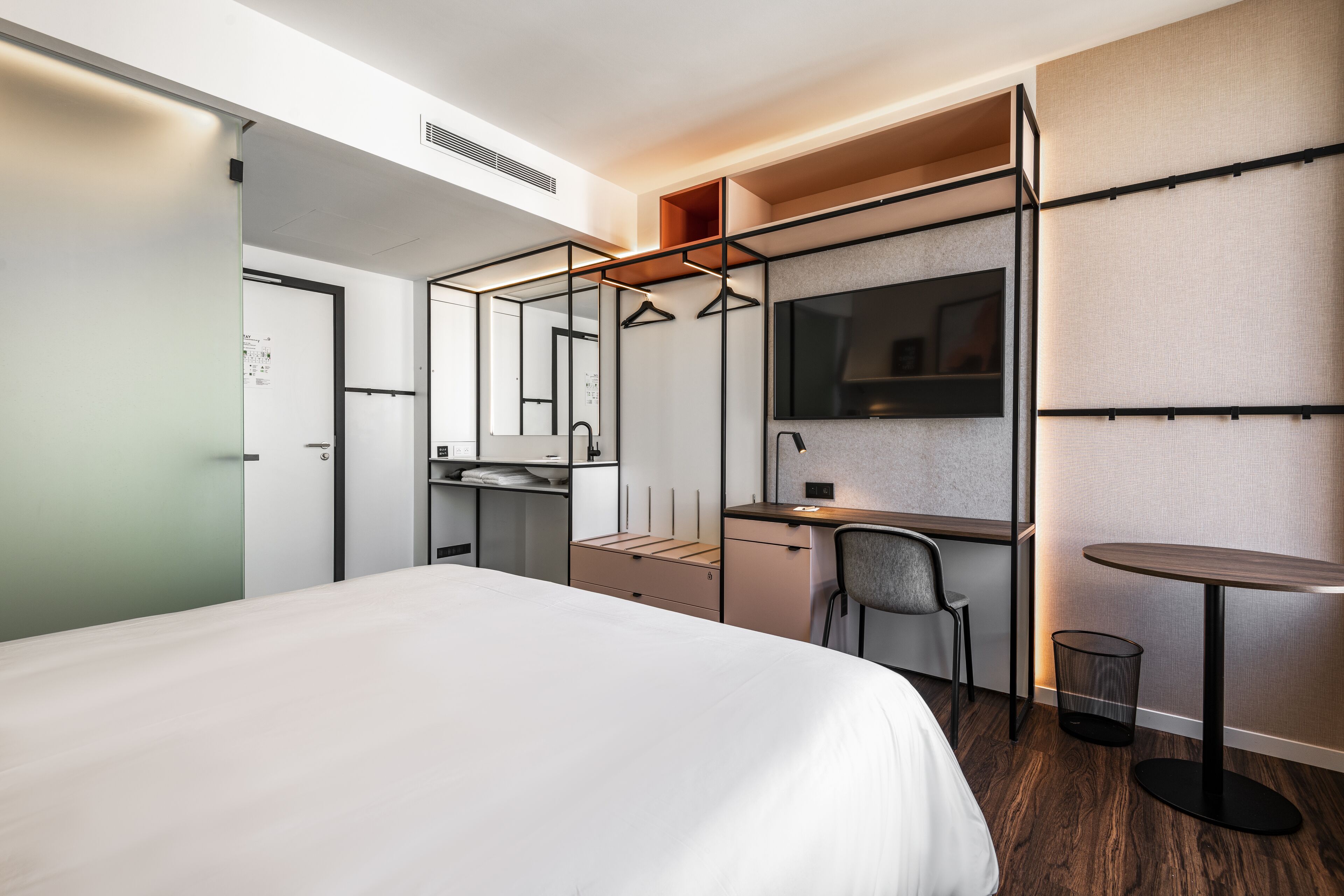 Une chambre d’hôtel moderne avec un grand lit, un bureau avec une chaise, une petite table et un miroir.