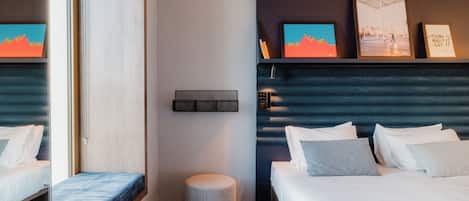 Ein Hotelzimmer mit Bett, Nachttisch und einem kleinen runden Hocker. Darüber befinden sich zwei Bilder an der Wand.