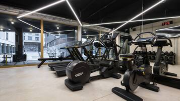 Een sportschool met diverse fitnessapparaten, een digitaal scherm en uitzicht naar buiten door grote ramen.